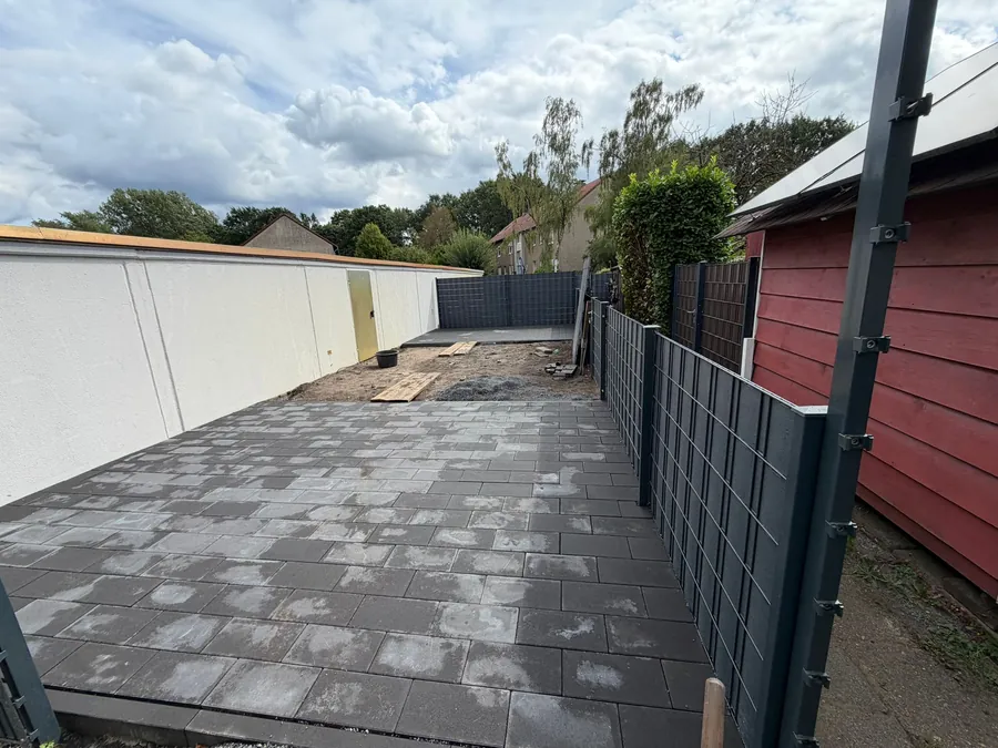Die fertige Terrasse aus grauen Betonplatten, verfugt und abgerüttelt, seitlich der anthrazitfarbene Zaun mit Sichtschutz