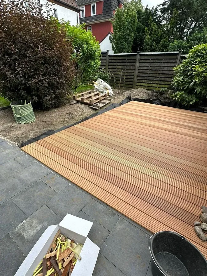 Frisch verlegte helle Holzdielen auf schwarzem Unkrautvlies, angrenzend an die vorhandenen Steinplatten
