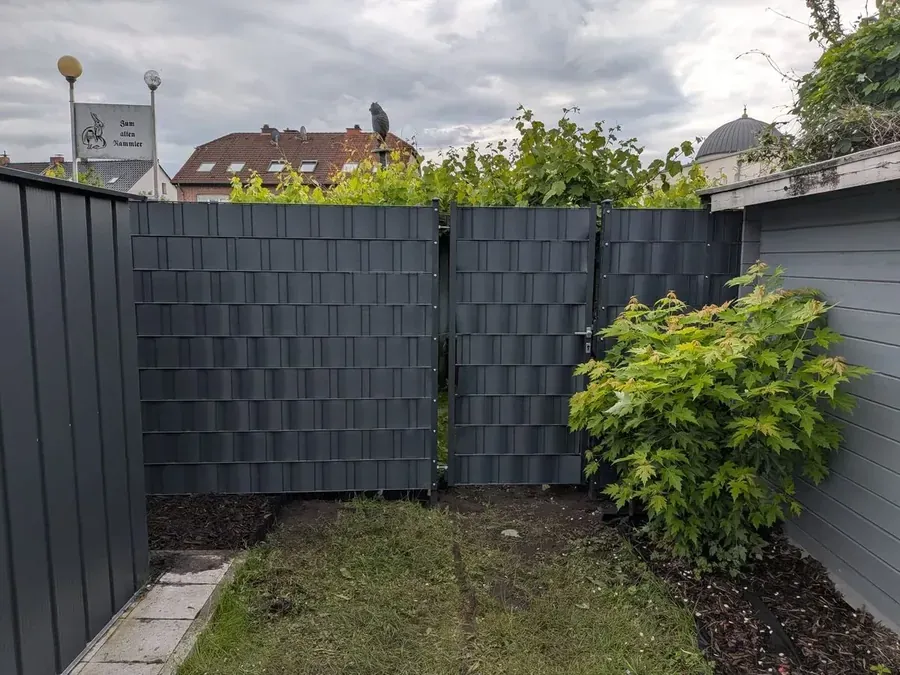 Dieselbe Ecke fertig: anthrazitfarbener Doppelstabmattenzaun mit Sichtschutzstreifen in zwei Höhen und abschließbarem Tor